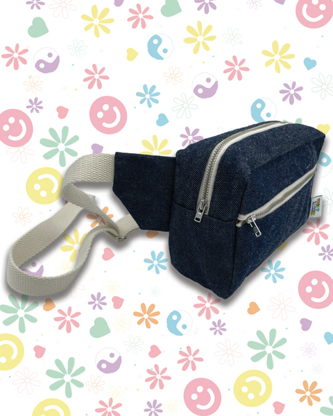 A dark blue denim bumbag with a light beige adjustable strap and zips. 