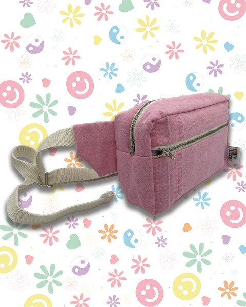 A pink denim bumbag  with a cream adjustable strap and silver zippers. 