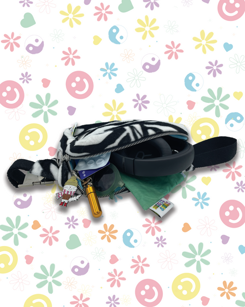 A black and white zebra-print bumbag shown open, filled with various accessories to show how much it can hold. 
