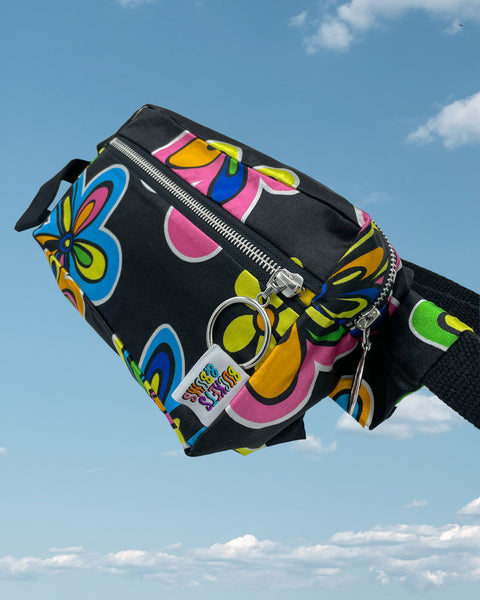 Product shot - silky black bumbag with large blue and pink neon flower pattern showing Buckets & Bums woven label